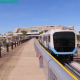 Gate Link train on an elevated guideway at Orlando International Airport, with palm trees, airport buildings and a control tower behind it.